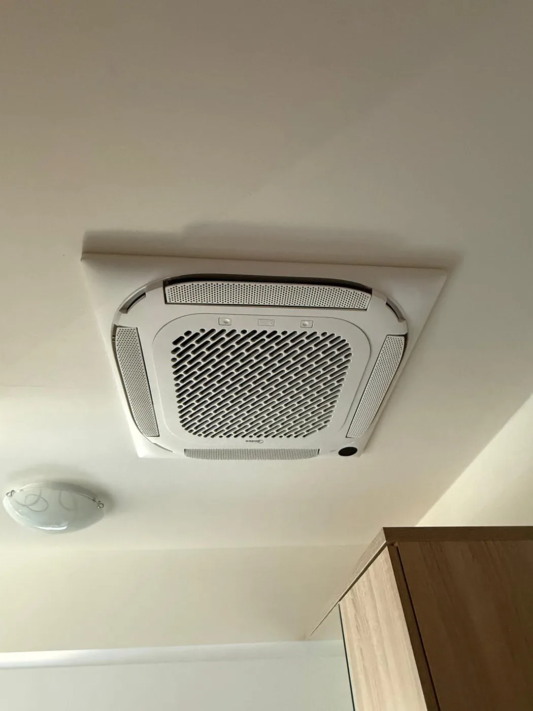 Kazetová klimatizace Midea zapuštěná do sádrokartonového podhledu vedle stropního svítidla